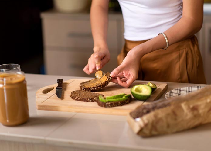 Woman spreading peanut butter and avocado on toast