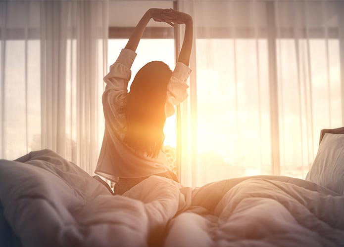 Woman stretching arms in bed with sunrise