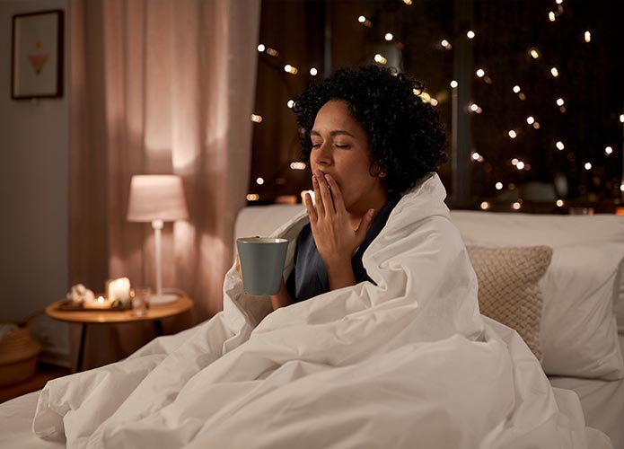 Woman sitting in bed with tea and yawning